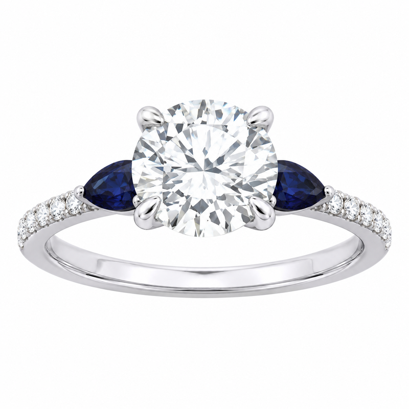 A white gold or platinum engagement ring featuring a round-cut center diamond, flanked by two marquise-cut deep blue sapphires and a pavé band of small clear diamonds on a white background.