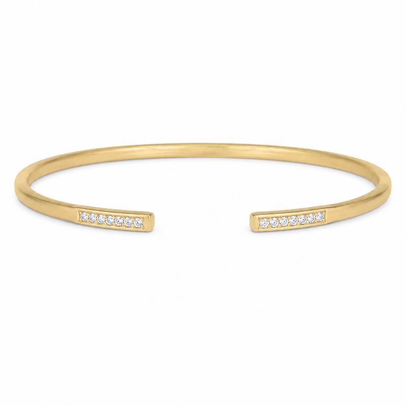 A modern take on the classic bangle, this 14K yellow gold design pairs a soft satin finish with 1/10 carat total weight of sparkling diamonds. Diamond-accented bars frame the open silhouette, creating a clean, contemporary look that’s beautiful worn alone or layered into a bracelet stack.
