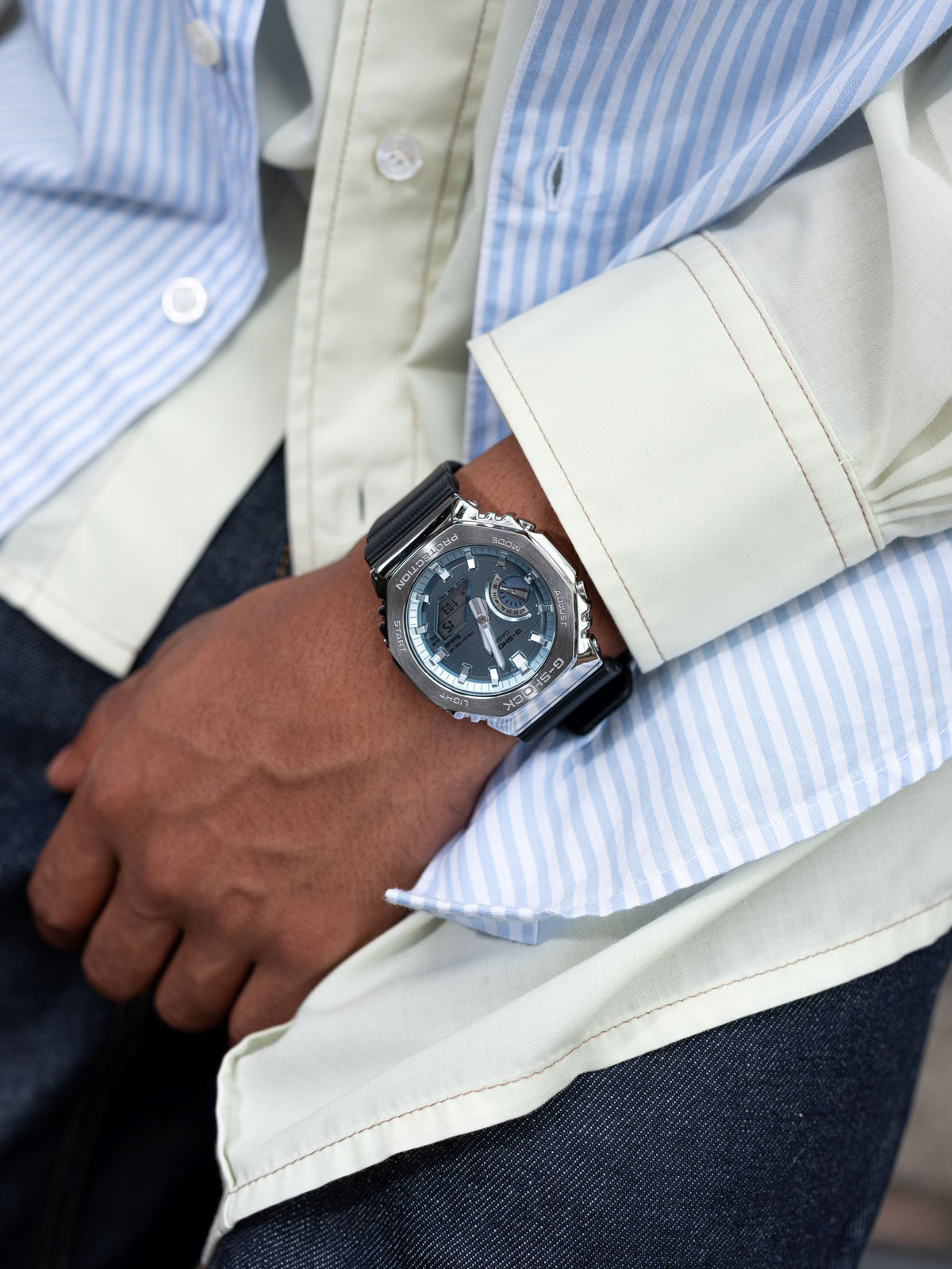 Close-up of a person wearing a watch with a blue and white striped shirt and beige jacket.