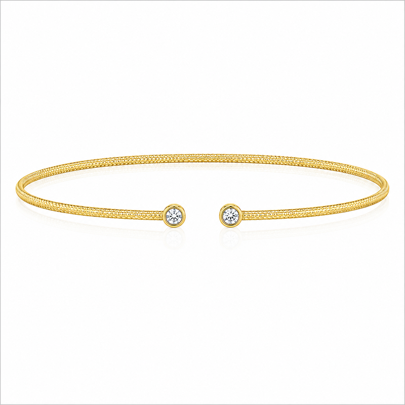 Two bezel-set round diamonds accent the open ends of a slender 14K yellow gold bangle. The diamonds total 1/10 carat total weight, while the textured finish adds subtle dimension to the design.